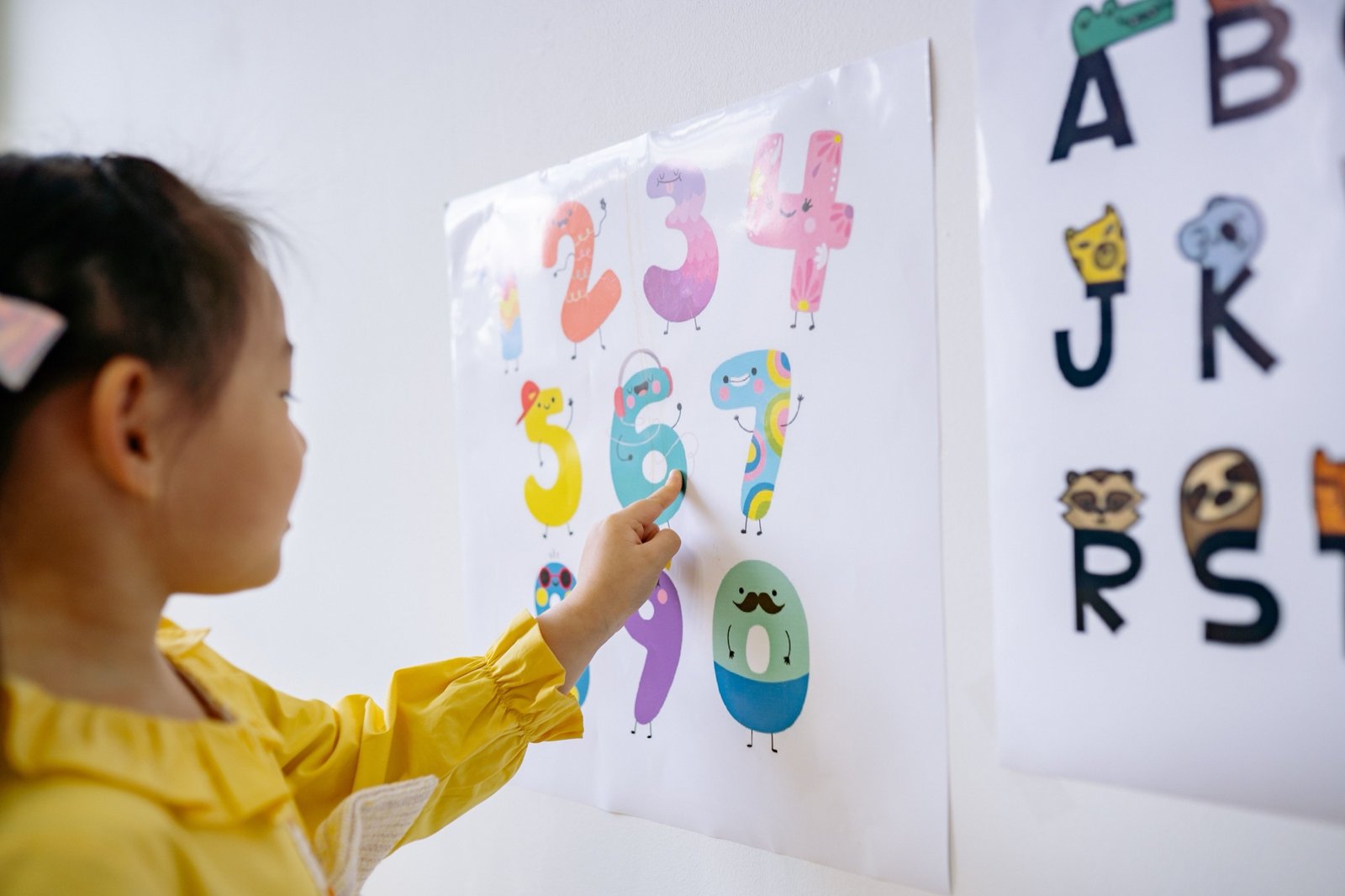 服務介紹 小女孩伸手指認牆上的數字與字母圖卡,透過視覺圖卡練習指認、辨識與表達,是 AAC 溝通輔具教學的常見活動